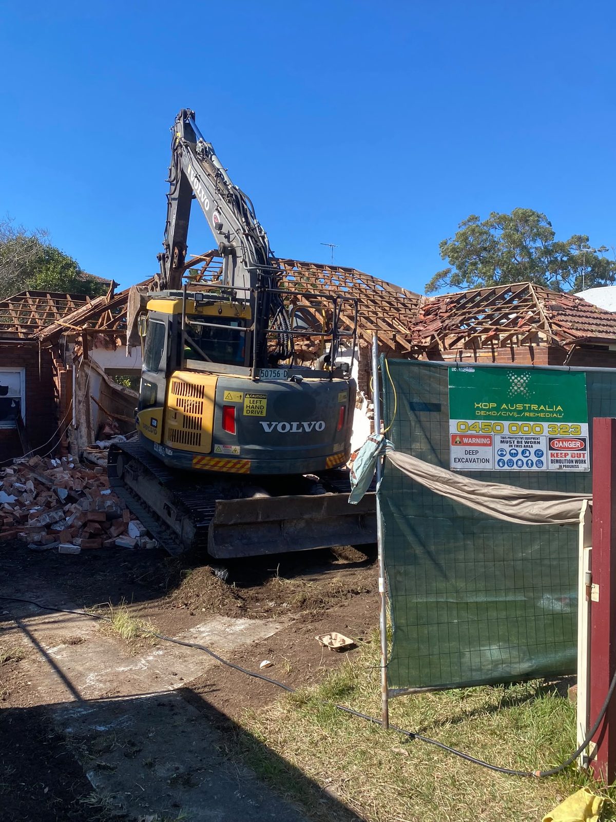 Excavator demolishing a house behind an XOP site sign
